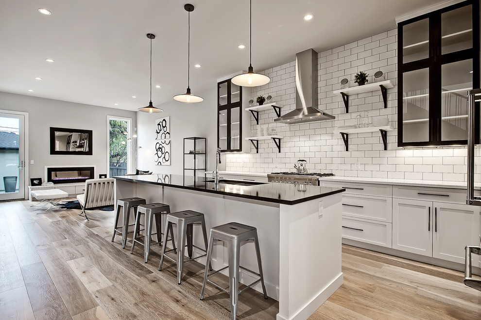 Photo of a traditional galley kitchen in Calgary with a submerged sink, shaker cabinets, white cabinets, engineered stone countertops, white splashback, ceramic splashback, stainless steel appliances, light hardwood flooring and an island.