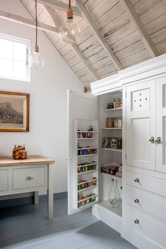 Modelo de cocina campestre con despensa, armarios con rebordes decorativos, puertas de armario blancas y suelo de madera pintada