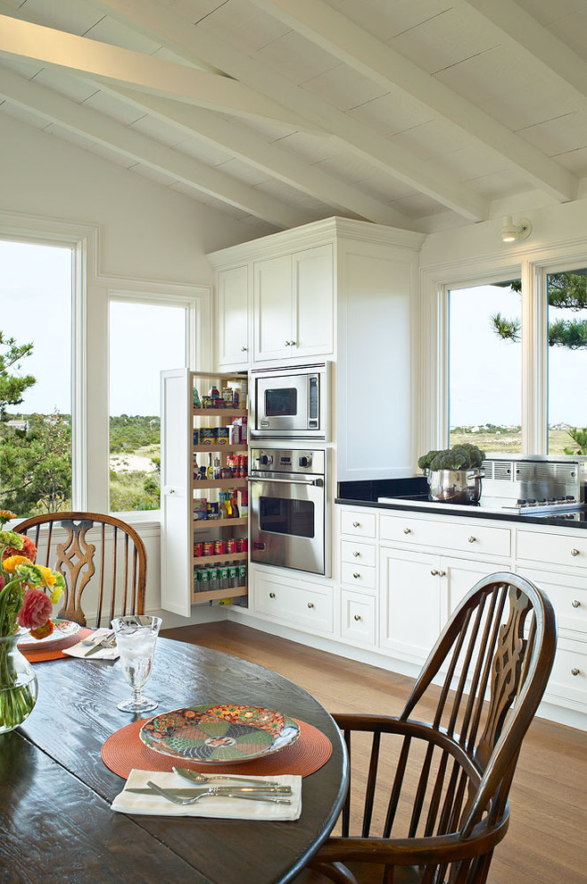 Foto på ett vintage kök och matrum, med rostfria vitvaror, skåp i shakerstil, vita skåp, mellanmörkt trägolv och en köksö