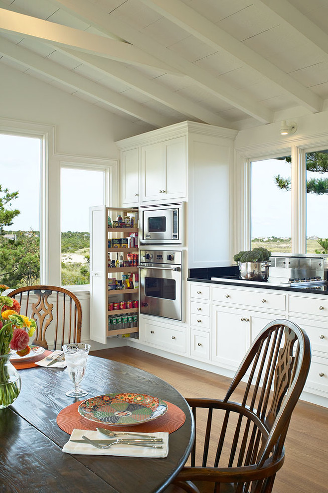 Example of a classic medium tone wood floor eat-in kitchen design in New York with stainless steel appliances, shaker cabinets, white cabinets and an island