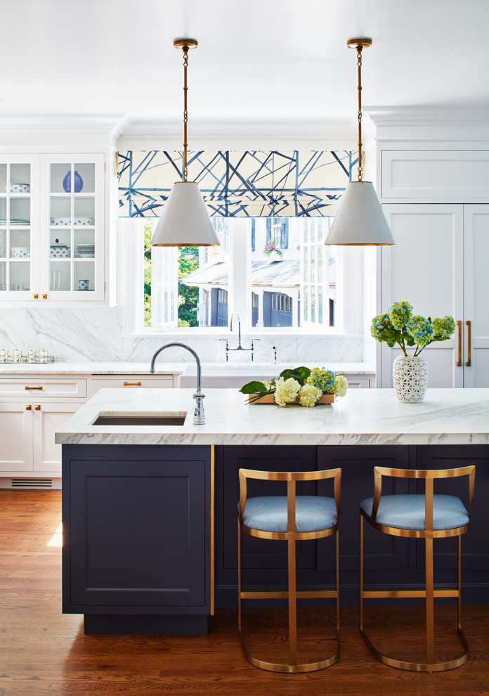Inspiration for a large transitional l-shaped medium tone wood floor kitchen remodel in New York with white cabinets, white backsplash, an island, white countertops, a farmhouse sink, shaker cabinets, marble countertops, marble backsplash and paneled appliances