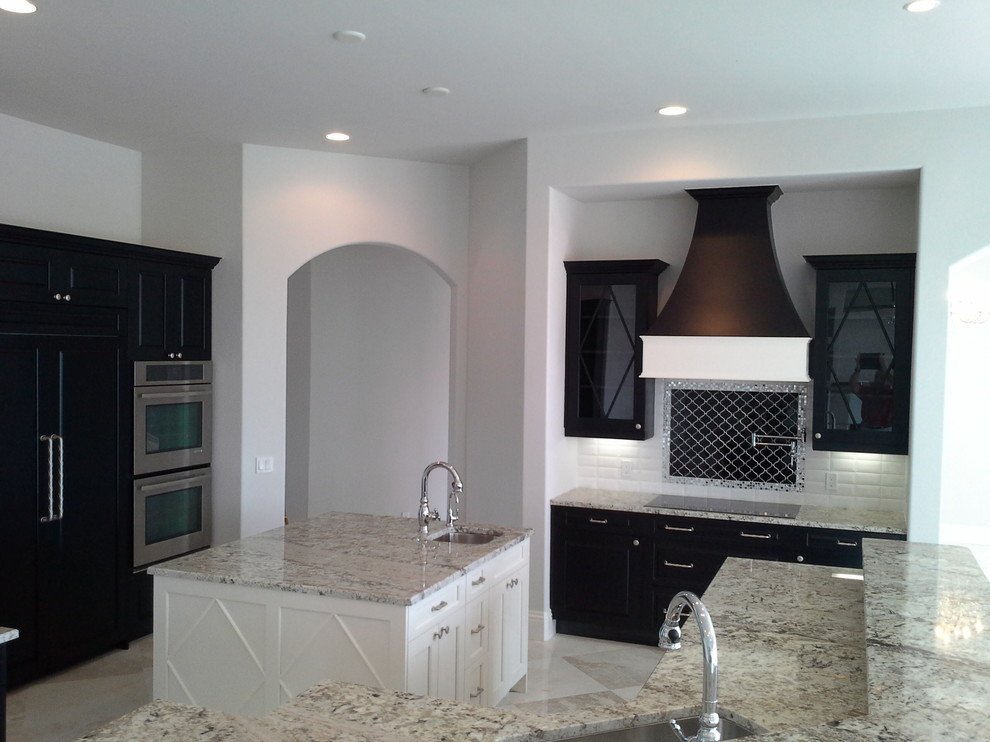Mid-sized elegant u-shaped marble floor eat-in kitchen photo in Miami with an undermount sink, recessed-panel cabinets, black cabinets, granite countertops, white backsplash, subway tile backsplash, stainless steel appliances and two islands