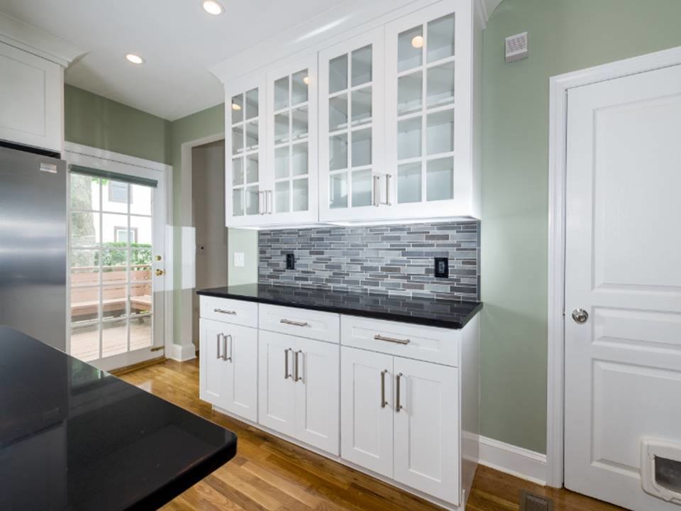 Inspiration for a large timeless medium tone wood floor enclosed kitchen remodel in New York with an undermount sink, shaker cabinets, white cabinets, granite countertops, multicolored backsplash, stone tile backsplash, stainless steel appliances and an island