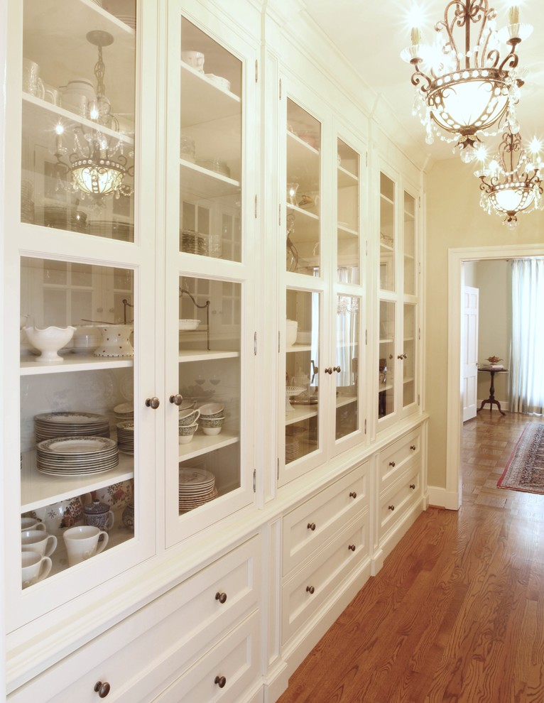 Cette image montre une grande arrière-cuisine parallèle et encastrable traditionnelle avec un placard à porte vitrée, des portes de placard blanches, plan de travail en marbre, une crédence blanche et un sol en bois brun.