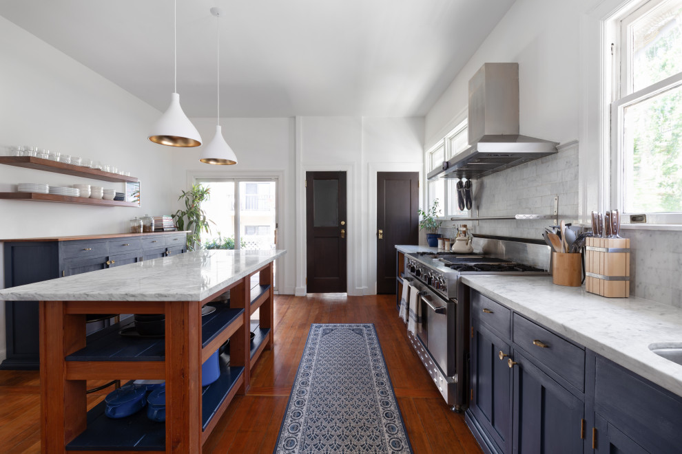 Inspiration for a transitional galley dark wood floor and brown floor enclosed kitchen remodel in San Francisco with an undermount sink, shaker cabinets, blue cabinets, stainless steel appliances, an island, white countertops, gray backsplash and ceramic backsplash