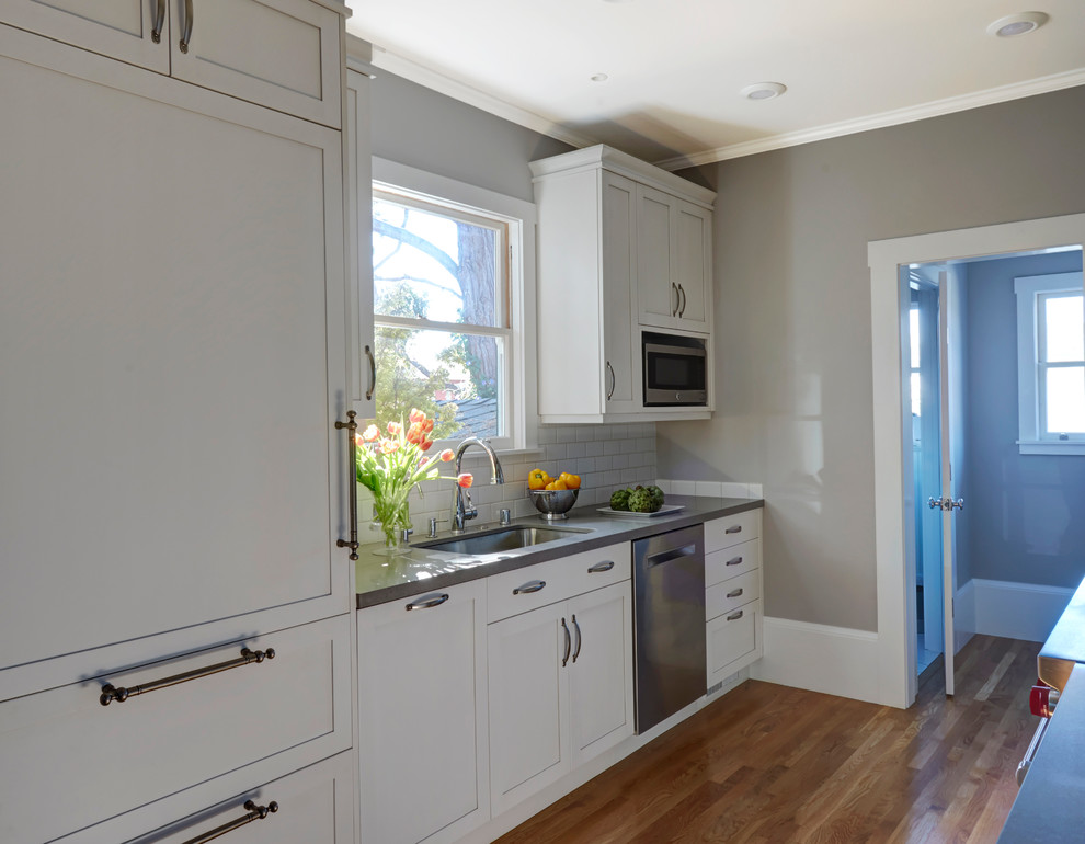 This is an example of a medium sized traditional galley enclosed kitchen in San Francisco with a submerged sink, shaker cabinets, white cabinets, engineered stone countertops, white splashback, metro tiled splashback, integrated appliances, light hardwood flooring and no island.