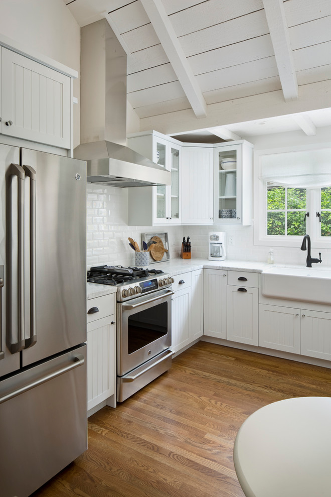 Mid-sized farmhouse l-shaped medium tone wood floor kitchen photo in Other with a farmhouse sink, recessed-panel cabinets, white cabinets, granite countertops, white backsplash, subway tile backsplash, stainless steel appliances and no island