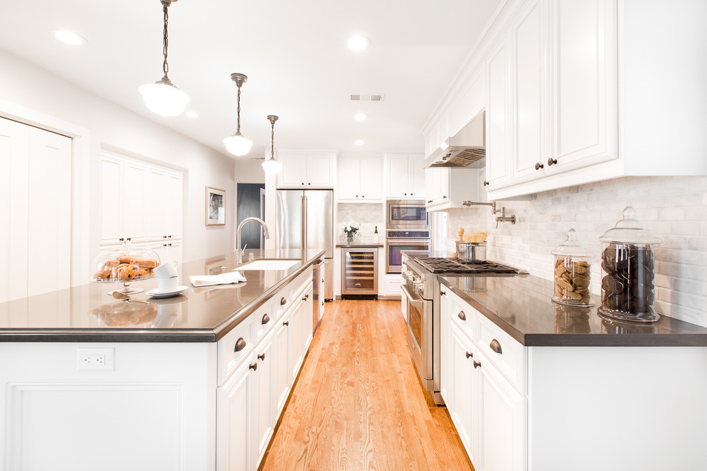 Exempel på ett klassiskt kök, med en undermonterad diskho, vita skåp, vitt stänkskydd, rostfria vitvaror, mellanmörkt trägolv och en köksö
