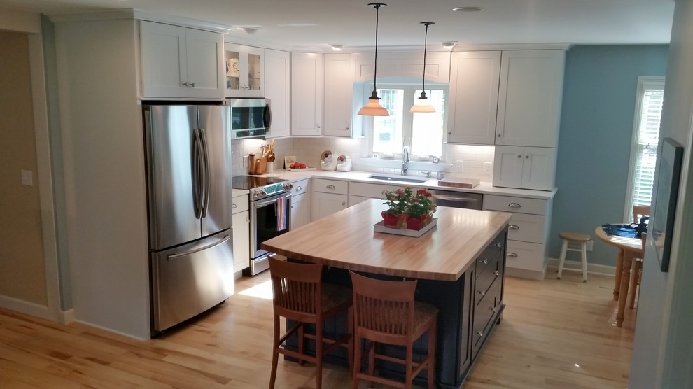 Mid-sized cottage chic l-shaped light wood floor eat-in kitchen photo in Charlotte with a drop-in sink, recessed-panel cabinets, quartz countertops, white backsplash, subway tile backsplash, stainless steel appliances and an island