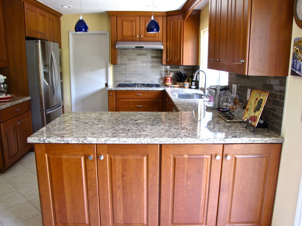 Foto på ett vintage kök, med en undermonterad diskho, luckor med infälld panel, skåp i mellenmörkt trä, granitbänkskiva, stänkskydd med metallisk yta, stänkskydd i cementkakel, rostfria vitvaror, klinkergolv i keramik och en halv köksö