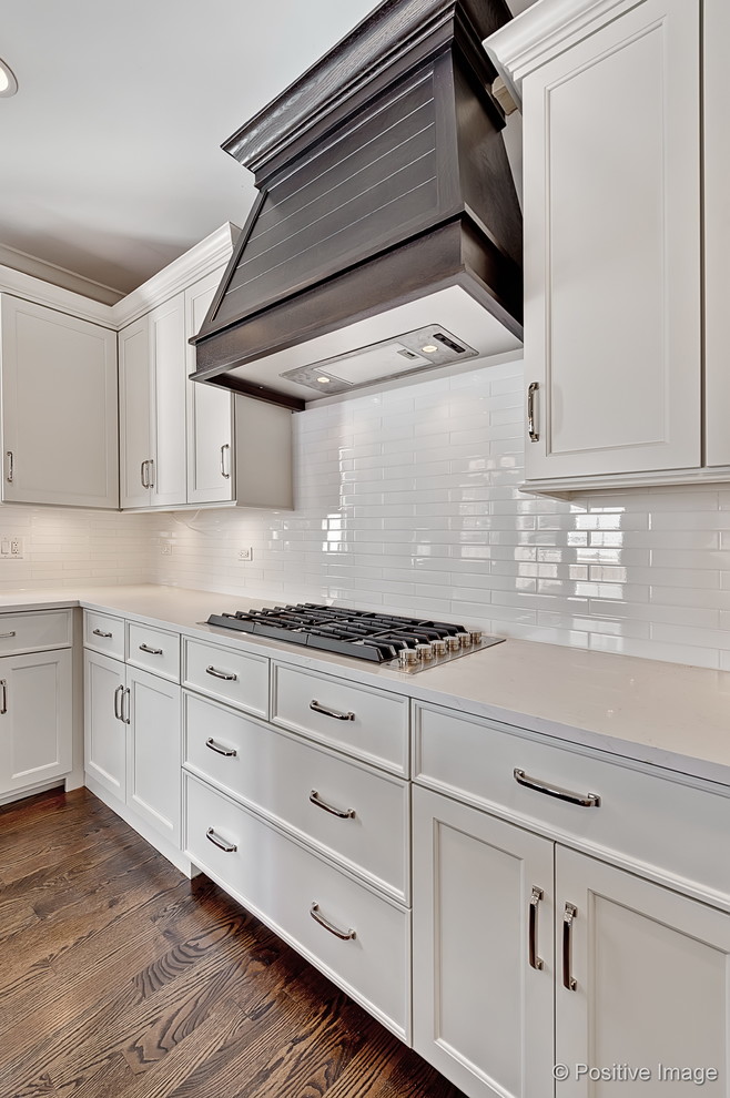 Inspiration for a large craftsman u-shaped light wood floor enclosed kitchen remodel in Chicago with an undermount sink, shaker cabinets, white cabinets, solid surface countertops, white backsplash, subway tile backsplash, stainless steel appliances and an island