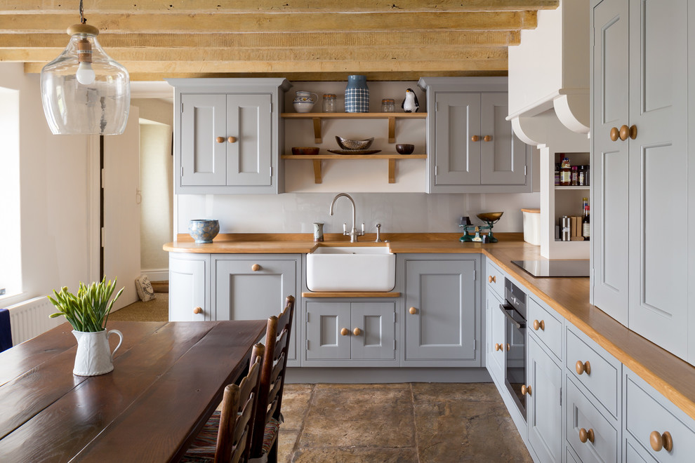 Design ideas for a rural l-shaped kitchen/diner in Other with a belfast sink, shaker cabinets, blue cabinets, wood worktops, black appliances, no island and brown floors.