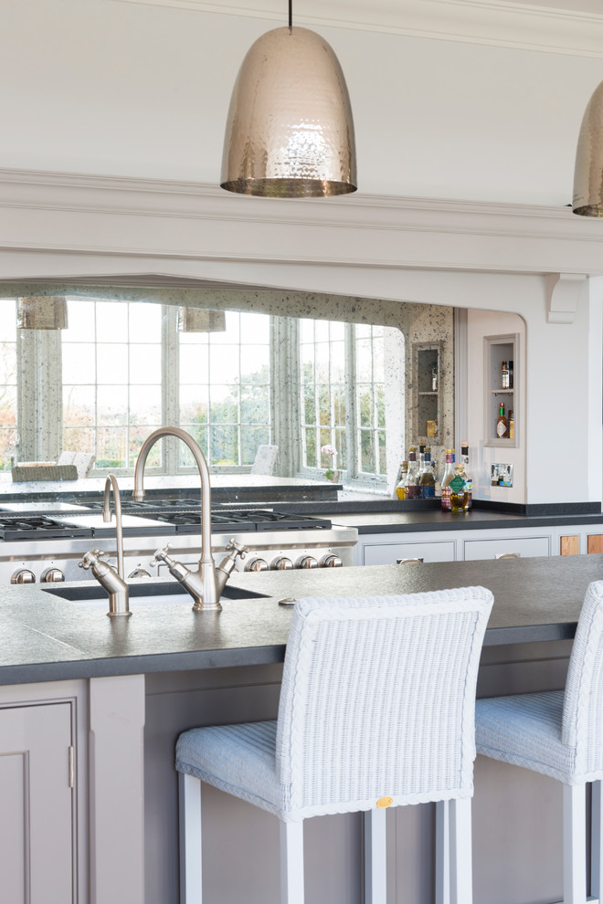 Foto på ett mycket stort vintage linjärt kök med öppen planlösning, med släta luckor, grå skåp, bänkskiva i kvartsit, stänkskydd med metallisk yta, en köksö, en rustik diskho, spegel som stänkskydd, rostfria vitvaror och kalkstensgolv