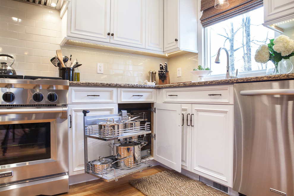 Example of a mid-sized classic u-shaped light wood floor eat-in kitchen design in New York with an undermount sink, raised-panel cabinets, white cabinets, quartz countertops, beige backsplash, subway tile backsplash, stainless steel appliances and a peninsula