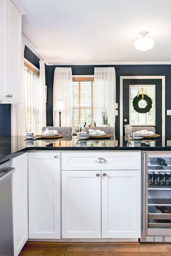 Inredning av ett lantligt avskilt, mellanstort svart svart u-kök, med en dubbel diskho, luckor med glaspanel, vita skåp, granitbänkskiva, grått stänkskydd, stänkskydd i marmor, rostfria vitvaror, mellanmörkt trägolv, en köksö och brunt golv