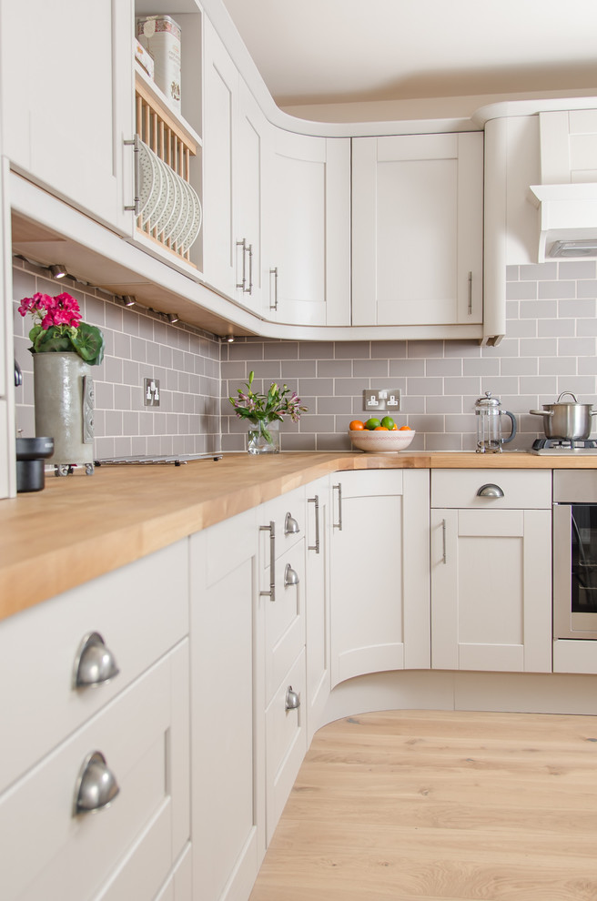 This is an example of a medium sized classic open plan kitchen in Other with a double-bowl sink, shaker cabinets, beige cabinets, wood worktops, grey splashback, ceramic splashback, stainless steel appliances and lino flooring.