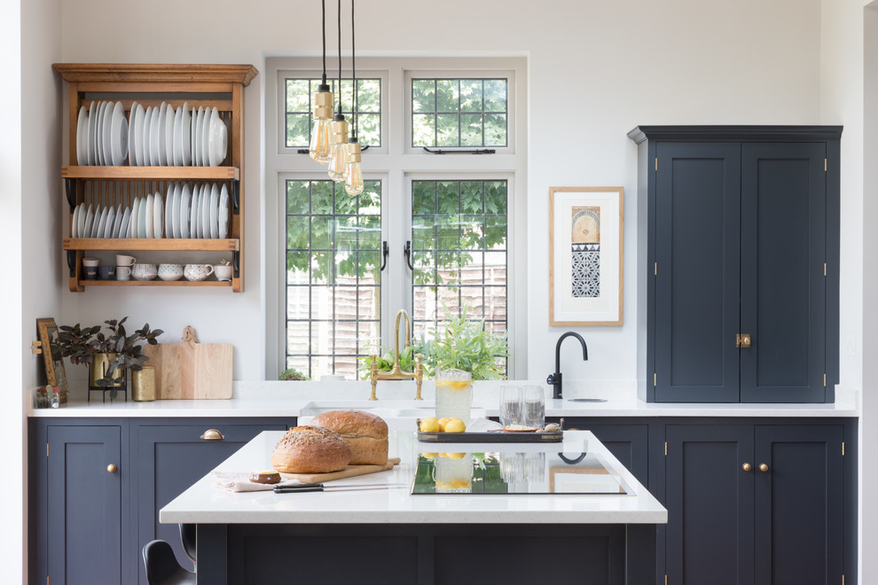 На фото: кухня в стиле неоклассика (современная классика) с фасадами в стиле шейкер, синими фасадами, островом, белой столешницей и окном