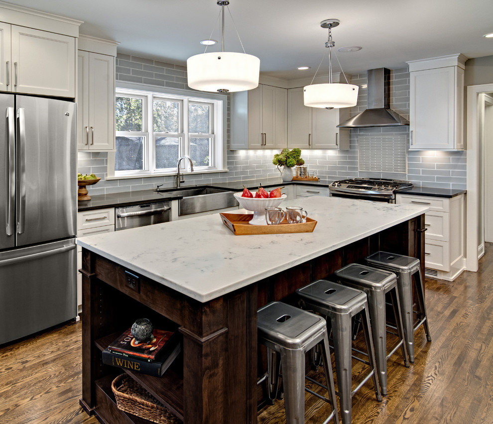 Medium sized traditional l-shaped kitchen/diner in Minneapolis with a belfast sink, shaker cabinets, white cabinets, marble worktops, blue splashback, metro tiled splashback, stainless steel appliances, medium hardwood flooring and an island.