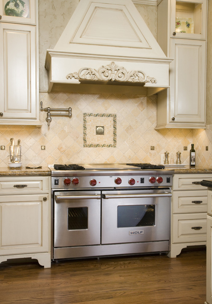 Klassisk inredning av ett kök, med luckor med upphöjd panel, rostfria vitvaror, beige skåp och stänkskydd i travertin