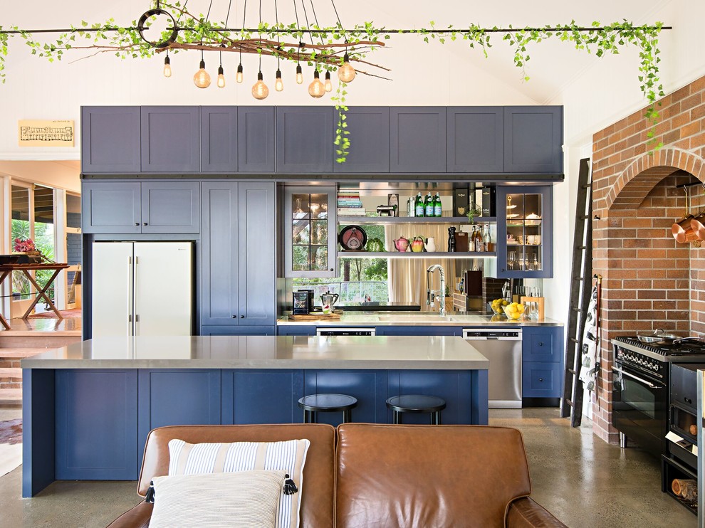 Offene Stilmix Küche in L-Form mit Schrankfronten im Shaker-Stil, blauen Schränken, Edelstahl-Arbeitsplatte, Küchengeräten aus Edelstahl, Betonboden, Kücheninsel und grauem Boden in Brisbane