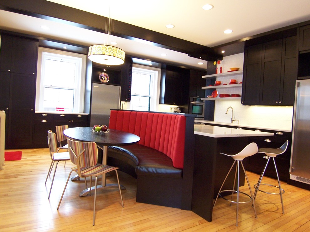Inredning av ett modernt kök och matrum, med skåp i shakerstil, svarta skåp, vitt stänkskydd, rostfria vitvaror, ljust trägolv och brunt golv