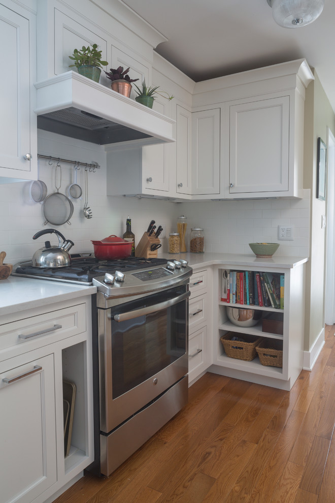Klassische Wohnküche mit weißen Schränken, Quarzwerkstein-Arbeitsplatte, Küchenrückwand in Weiß, Küchengeräten aus Edelstahl, hellem Holzboden und Halbinsel in New York