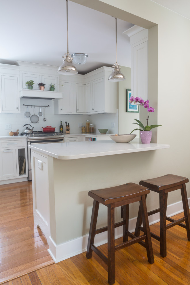 Klassische Wohnküche mit weißen Schränken, Quarzwerkstein-Arbeitsplatte, Küchenrückwand in Weiß, Küchengeräten aus Edelstahl, hellem Holzboden und Halbinsel in New York