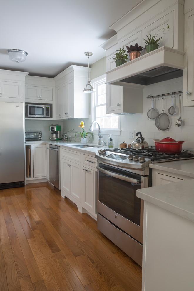 Immagine di una cucina abitabile classica con top in quarzo composito, elettrodomestici in acciaio inossidabile, parquet chiaro e penisola