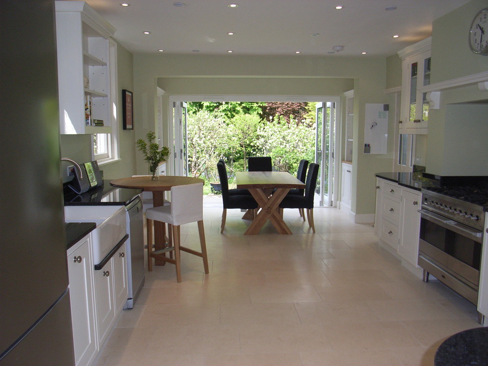 This is an example of a medium sized contemporary u-shaped open plan kitchen in Other with a belfast sink, shaker cabinets, white cabinets, granite worktops, stainless steel appliances and travertine flooring.