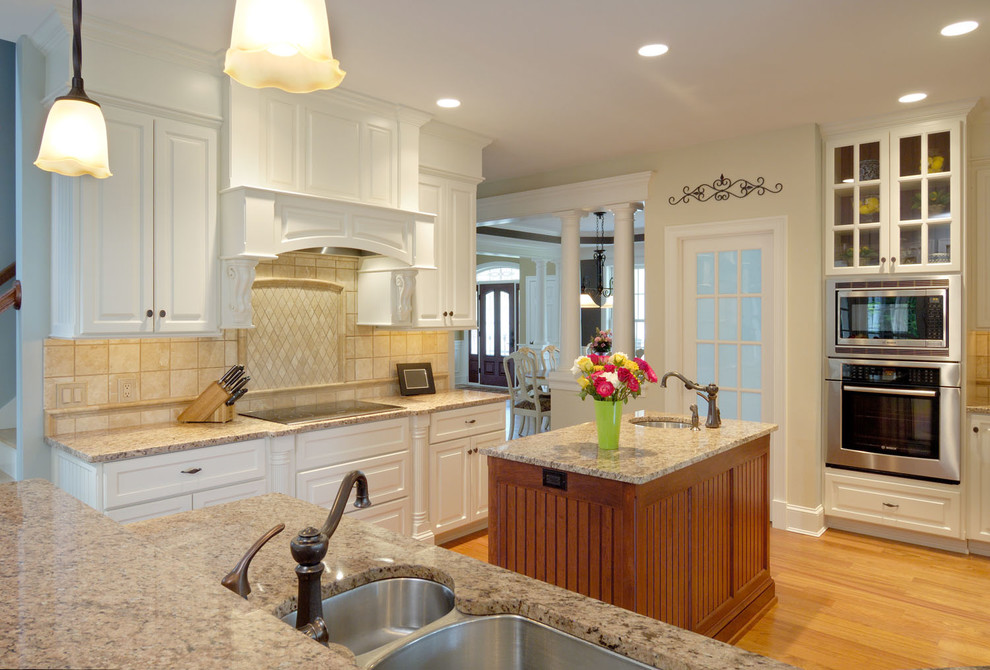 Bild på ett mellanstort lantligt kök, med en undermonterad diskho, vita skåp, granitbänkskiva, beige stänkskydd, ljust trägolv, flera köksöar, luckor med upphöjd panel, stänkskydd i keramik och rostfria vitvaror