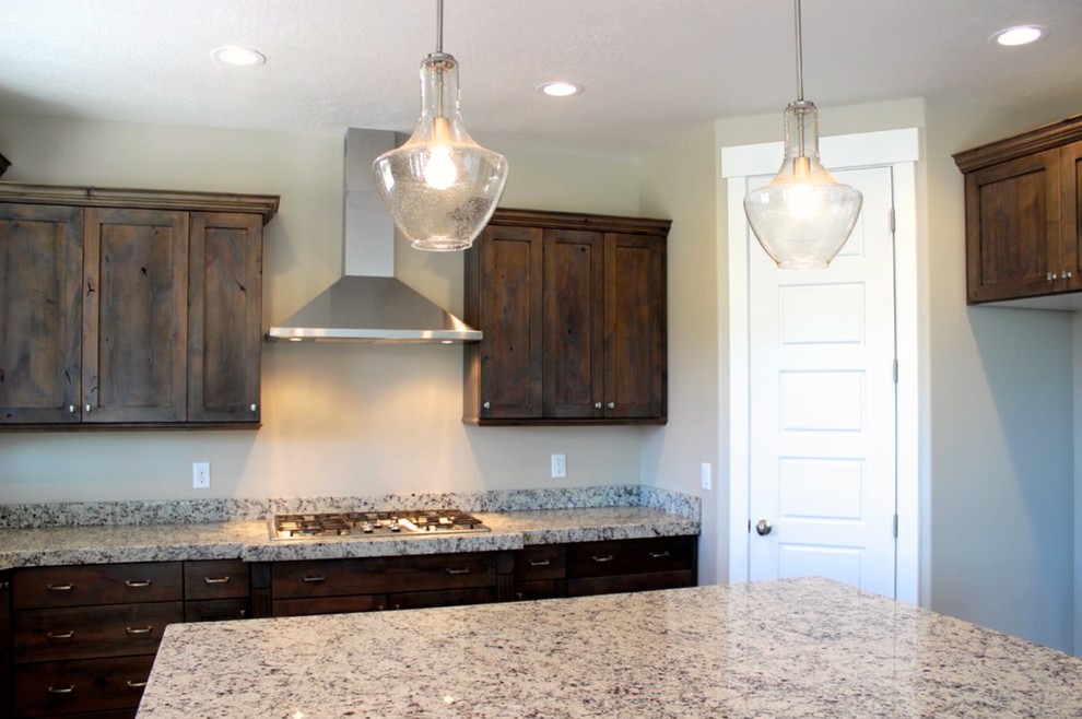 This is an example of a medium sized classic u-shaped open plan kitchen in Las Vegas with a double-bowl sink, shaker cabinets, dark wood cabinets, granite worktops, beige splashback, stainless steel appliances, dark hardwood flooring and an island.