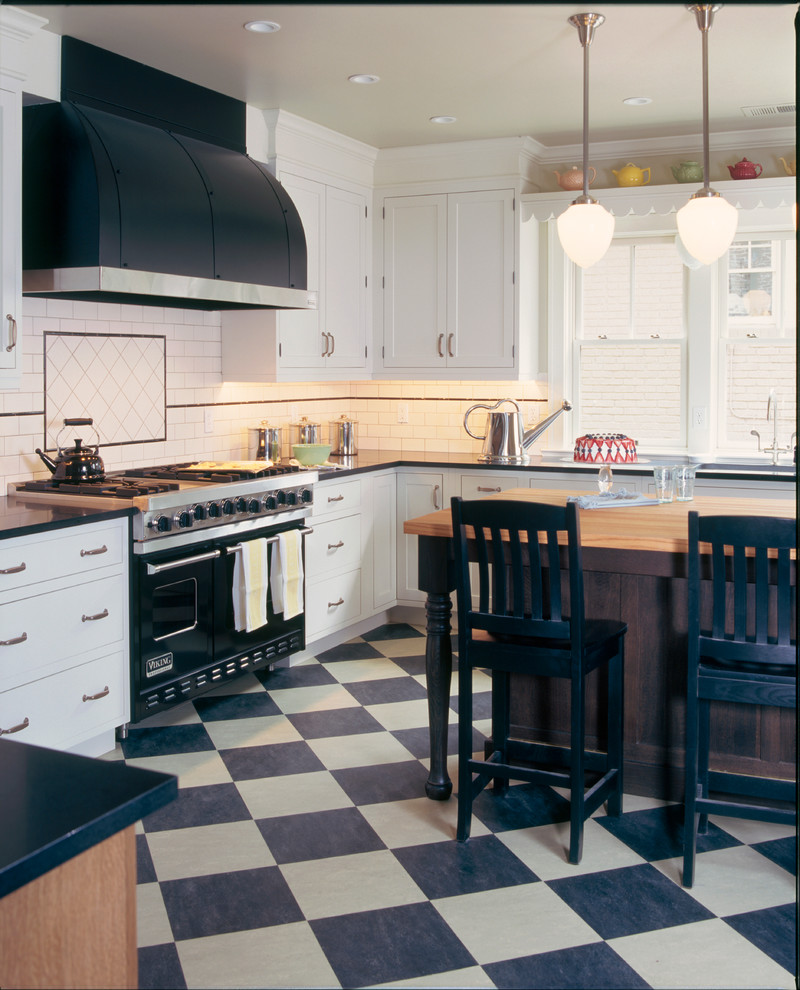 Inredning av ett klassiskt avskilt, mellanstort svart svart l-kök, med en undermonterad diskho, skåp i shakerstil, vita skåp, granitbänkskiva, vitt stänkskydd, stänkskydd i tunnelbanekakel, svarta vitvaror, linoleumgolv och en köksö