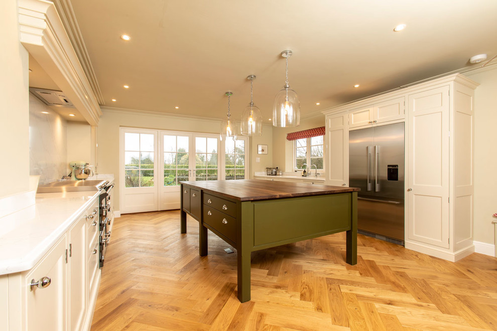 Photo of a large traditional u-shaped enclosed kitchen in Wiltshire with a submerged sink, white cabinets, white splashback, marble splashback, stainless steel appliances, medium hardwood flooring, an island and brown floors.