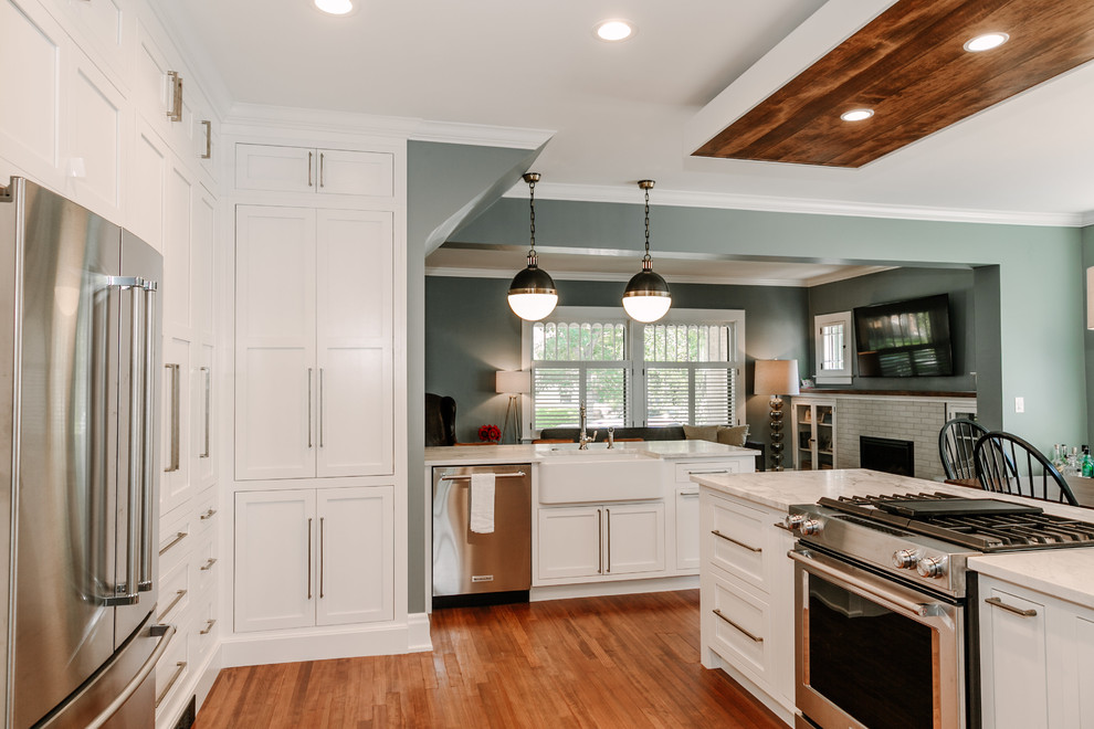 Photo of a medium sized traditional u-shaped kitchen/diner in Denver with a belfast sink, shaker cabinets, white cabinets, composite countertops, stainless steel appliances and dark hardwood flooring.