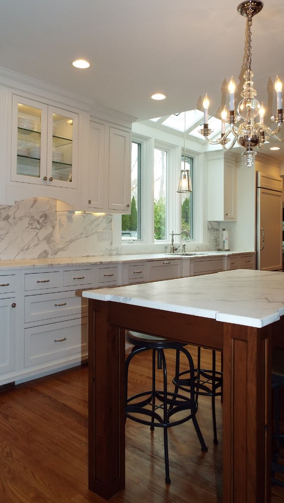 Klassisk inredning av ett mellanstort kök, med en enkel diskho, luckor med infälld panel, vita skåp, marmorbänkskiva, vitt stänkskydd, stänkskydd i sten, rostfria vitvaror, ljust trägolv och flera köksöar