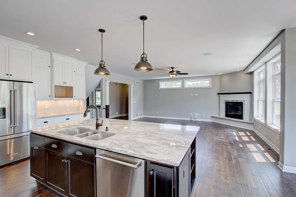 Inspiration for a large transitional l-shaped dark wood floor and brown floor enclosed kitchen remodel in Milwaukee with a triple-bowl sink, shaker cabinets, white cabinets, marble countertops, stainless steel appliances and an island