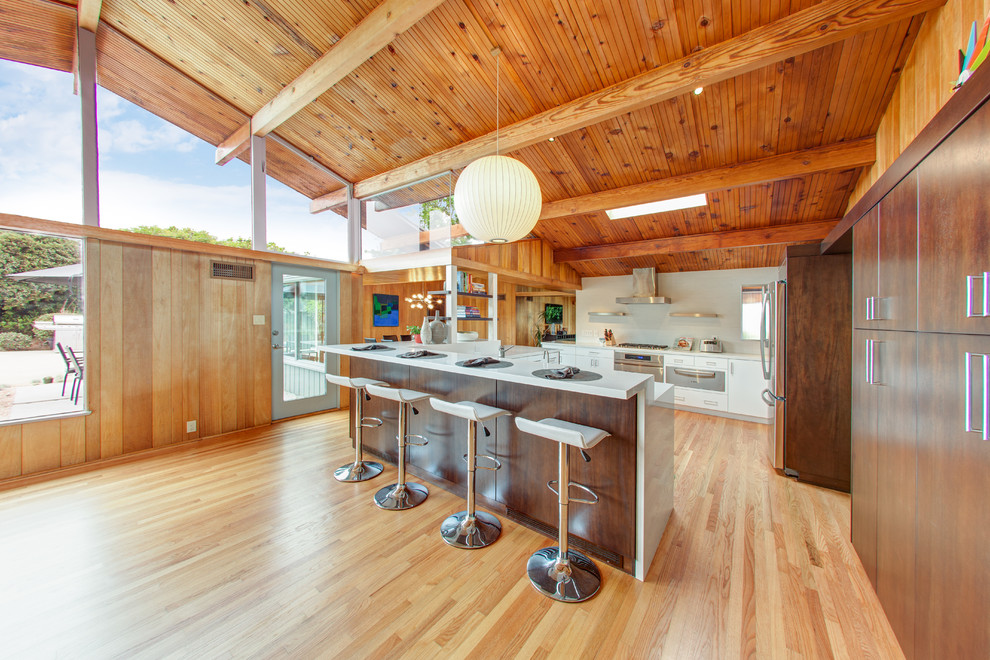 Cette image montre une cuisine design en bois foncé avec un placard à porte plane, une crédence blanche et un électroménager en acier inoxydable.