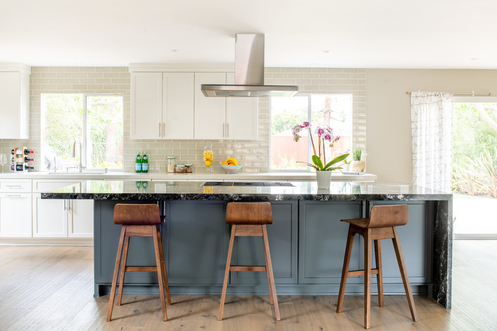 Design ideas for a medium sized contemporary single-wall kitchen/diner in Los Angeles with shaker cabinets, white cabinets, beige splashback, metro tiled splashback, light hardwood flooring, an island, beige floors and multicoloured worktops.