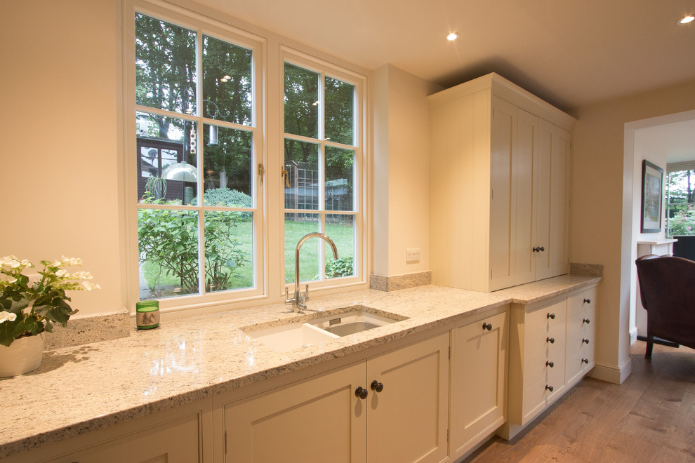 Huge elegant l-shaped medium tone wood floor open concept kitchen photo in Hertfordshire with a farmhouse sink, shaker cabinets, white cabinets, granite countertops, stainless steel appliances, two islands and white countertops