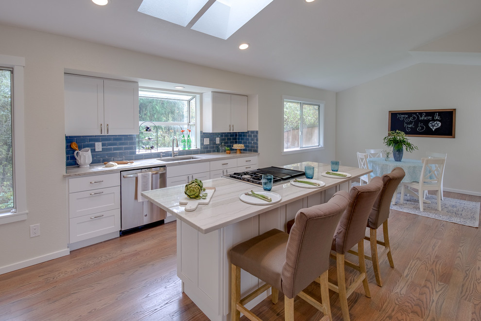 This is an example of a large modern galley kitchen/diner in Seattle with a submerged sink, shaker cabinets, white cabinets, quartz worktops, blue splashback, glass tiled splashback, stainless steel appliances, dark hardwood flooring, an island, brown floors and beige worktops.