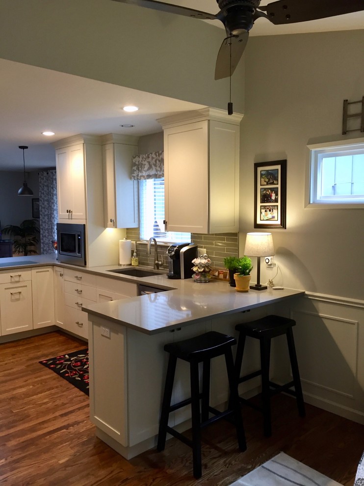 Small u-shaped medium tone wood floor open concept kitchen photo in Portland with an undermount sink, shaker cabinets, white cabinets, quartz countertops, gray backsplash, glass tile backsplash, stainless steel appliances, a peninsula and gray countertops