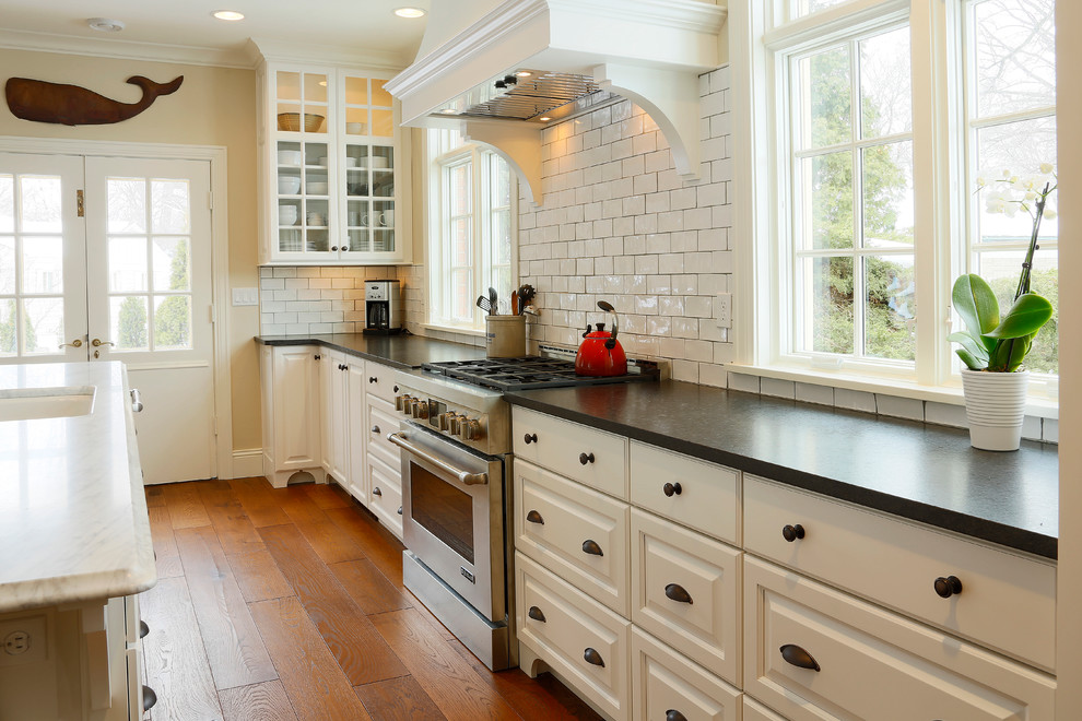 Example of a large transitional l-shaped medium tone wood floor eat-in kitchen design in Other with raised-panel cabinets, white cabinets, marble countertops, white backsplash, ceramic backsplash, stainless steel appliances and an island