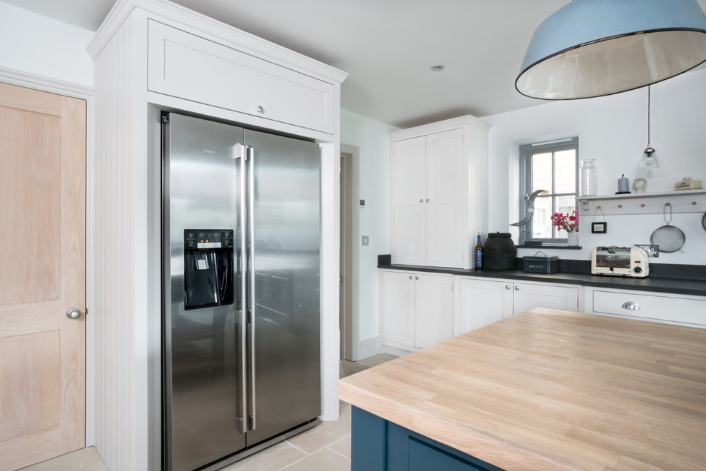 This is an example of an expansive country u-shaped open plan kitchen in Essex with a belfast sink, shaker cabinets, grey cabinets, granite worktops, white splashback, black appliances, terracotta flooring, an island, beige floors and black worktops.