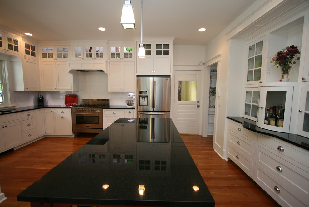 Photo of a medium sized traditional u-shaped enclosed kitchen in Seattle with a submerged sink, glass-front cabinets, white cabinets, granite worktops, white splashback, metro tiled splashback, stainless steel appliances, medium hardwood flooring and an island.