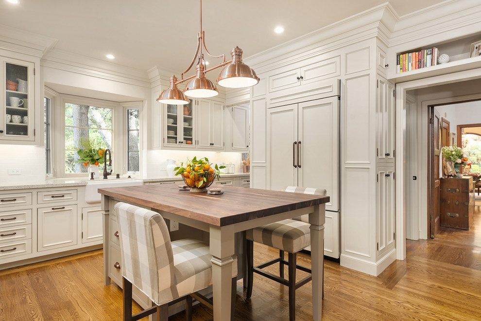 Mid-sized tuscan l-shaped medium tone wood floor and brown floor open concept kitchen photo in San Francisco with a farmhouse sink, recessed-panel cabinets, white cabinets, terrazzo countertops, white backsplash, subway tile backsplash, paneled appliances, an island and beige countertops
