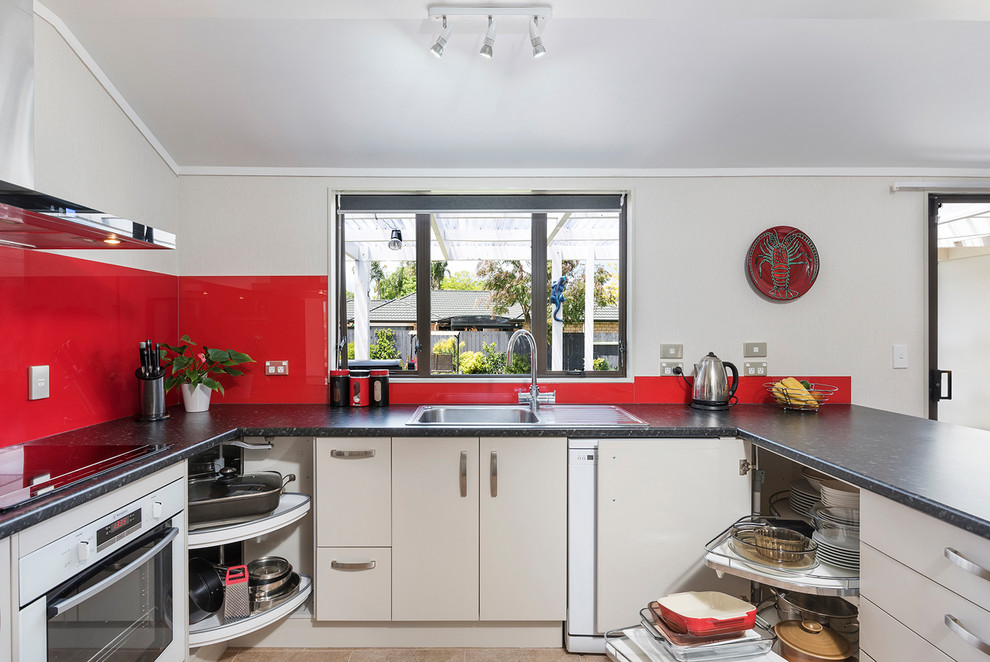 Inspiration for a medium sized contemporary u-shaped kitchen/diner in Auckland with a single-bowl sink, laminate countertops, red splashback, glass sheet splashback, porcelain flooring, beige floors, flat-panel cabinets, beige cabinets and a breakfast bar.