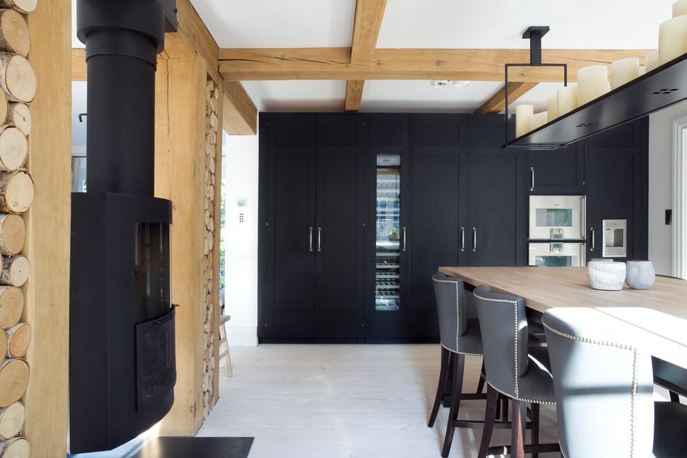 Große Nordische Wohnküche mit Landhausspüle, Schrankfronten im Shaker-Stil, schwarzen Schränken, Marmor-Arbeitsplatte, Küchenrückwand in Weiß, Rückwand aus Marmor, Elektrogeräten mit Frontblende, hellem Holzboden und Kücheninsel in Surrey