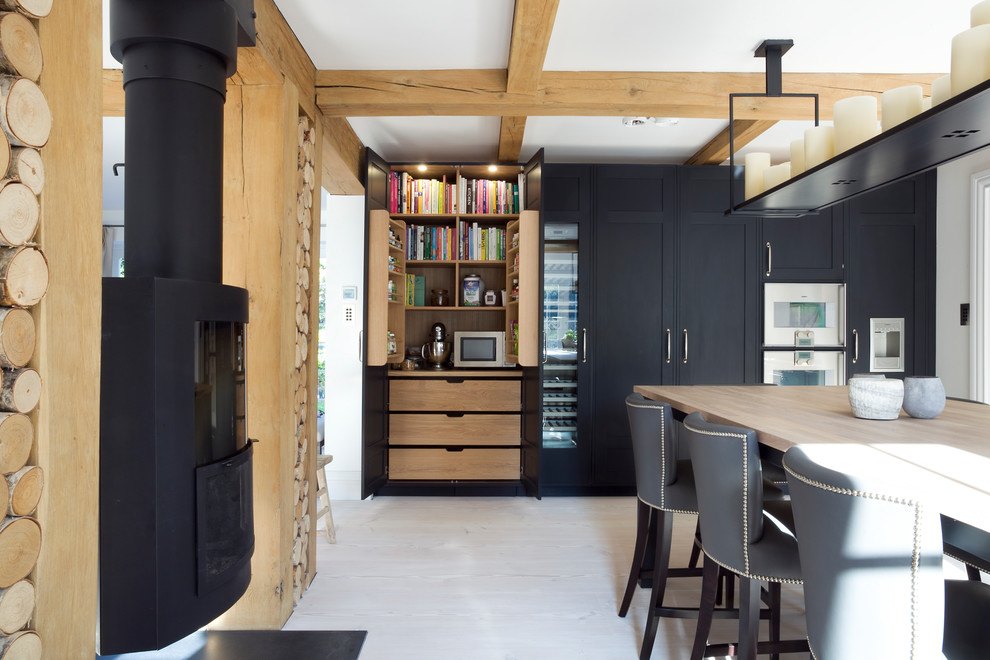 Photo of a large scandi kitchen in Surrey with shaker cabinets, black cabinets, integrated appliances, light hardwood flooring, an island, wood worktops and beige floors.