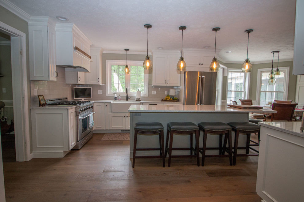 Inredning av ett klassiskt stort flerfärgad flerfärgat kök, med en rustik diskho, släta luckor, vita skåp, bänkskiva i kvarts, grått stänkskydd, stänkskydd i glaskakel, rostfria vitvaror, mellanmörkt trägolv, en köksö och brunt golv
