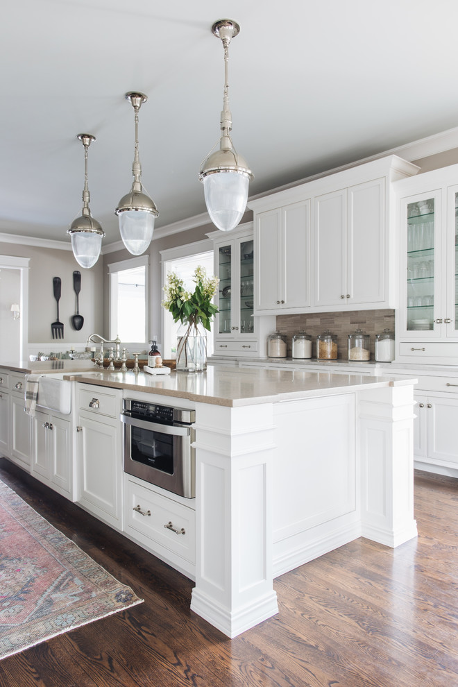 Classic kitchen in Chicago with a belfast sink, shaker cabinets, white cabinets, stainless steel appliances, dark hardwood flooring, an island, brown floors and beige worktops.